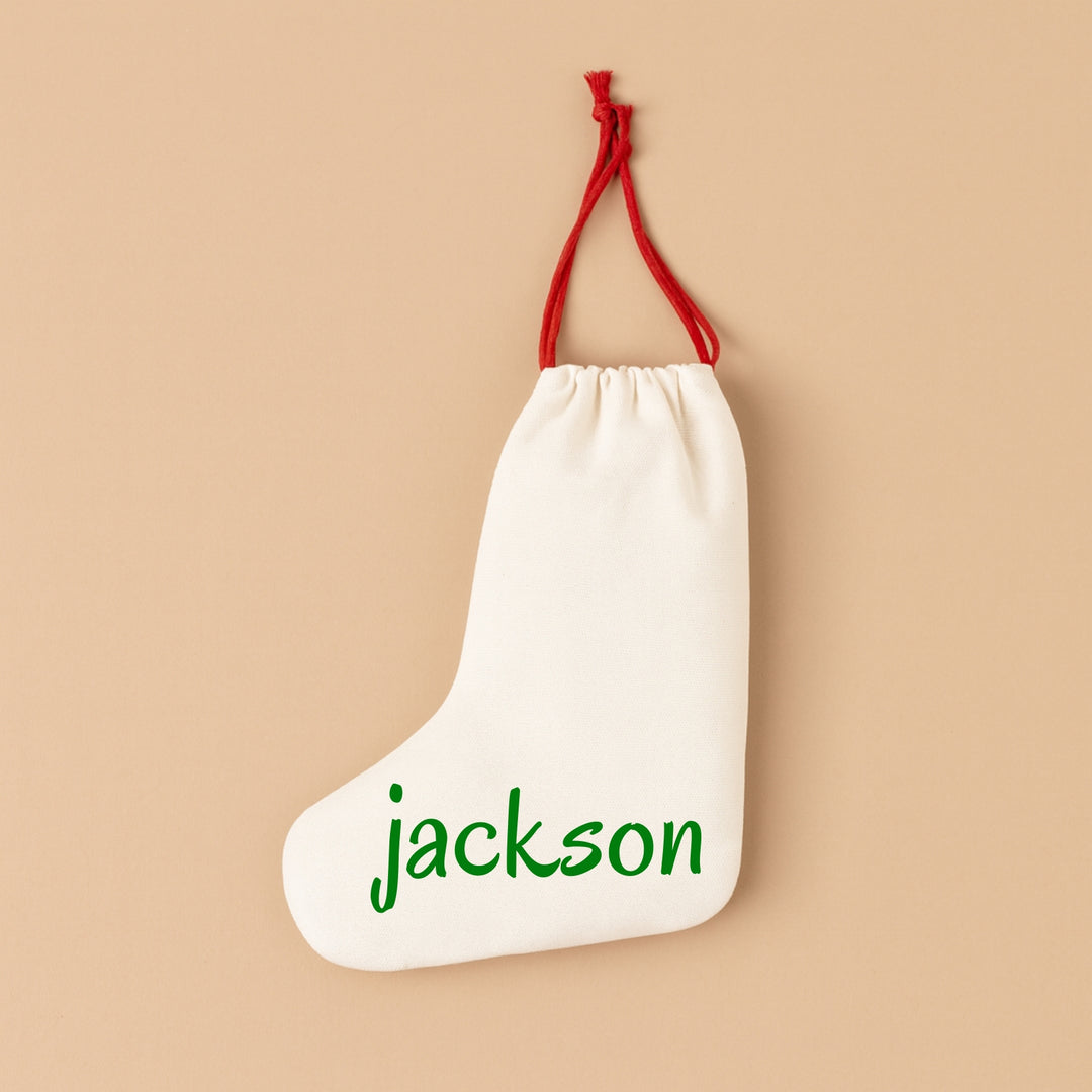 Personalized holiday stocking in cream fabric with green text displaying the name Jackson