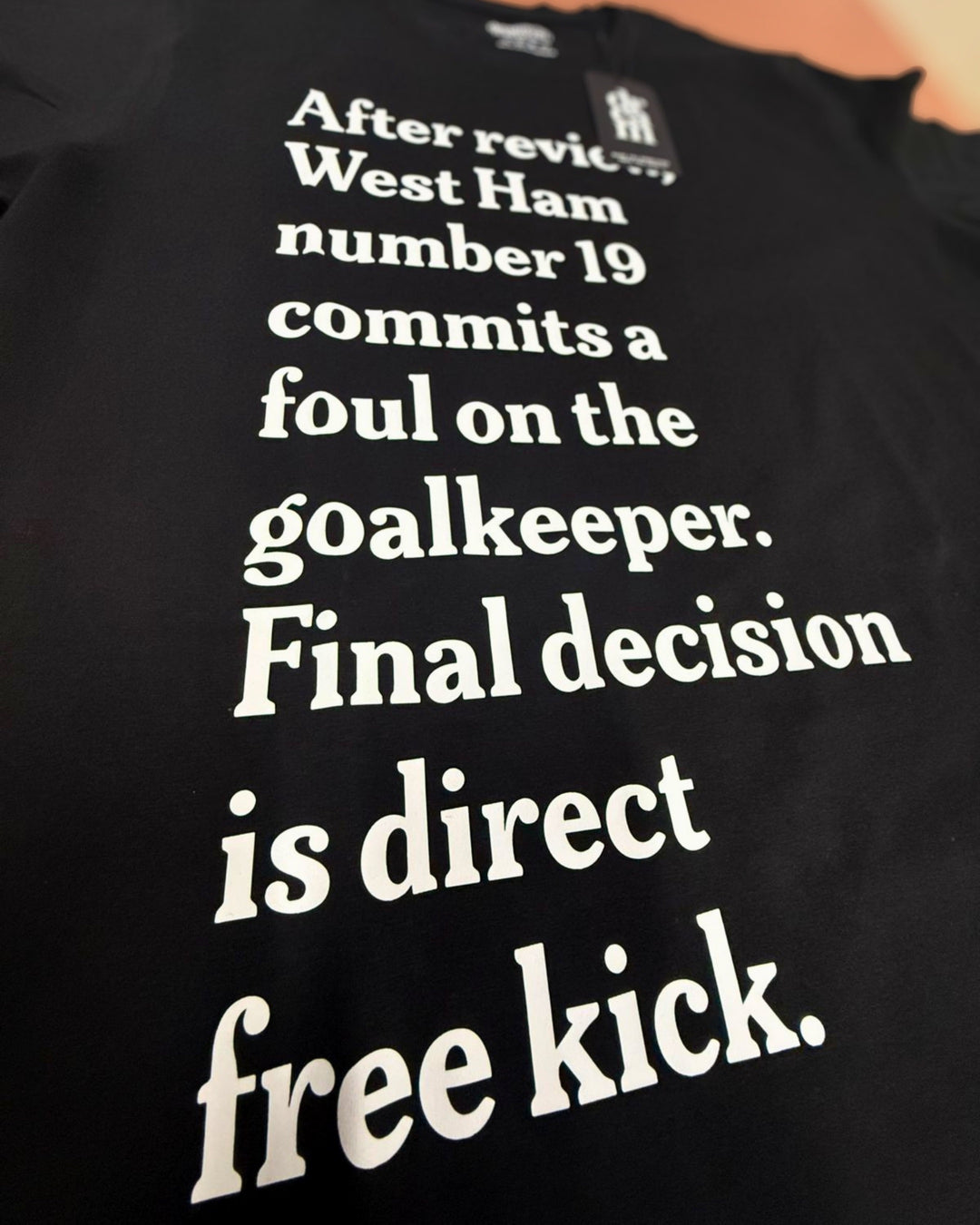 A close-up of a black t-shirt featuring a humorous football/soccer quote printed in white serif text: 'After review.