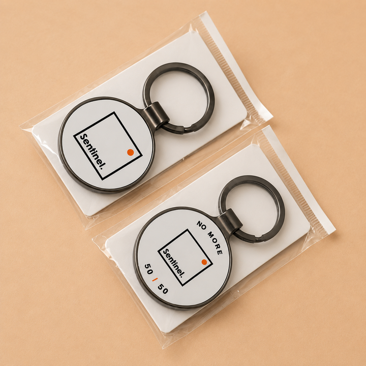 Two round black metal keychains with white circular inserts, each printed with a simple geometric design and the word &