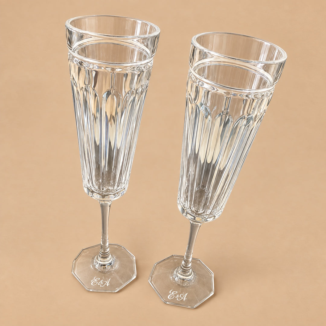 Two clear cut-glass champagne flutes with vertical ribbing and octagonal bases, each engraved with the initials &