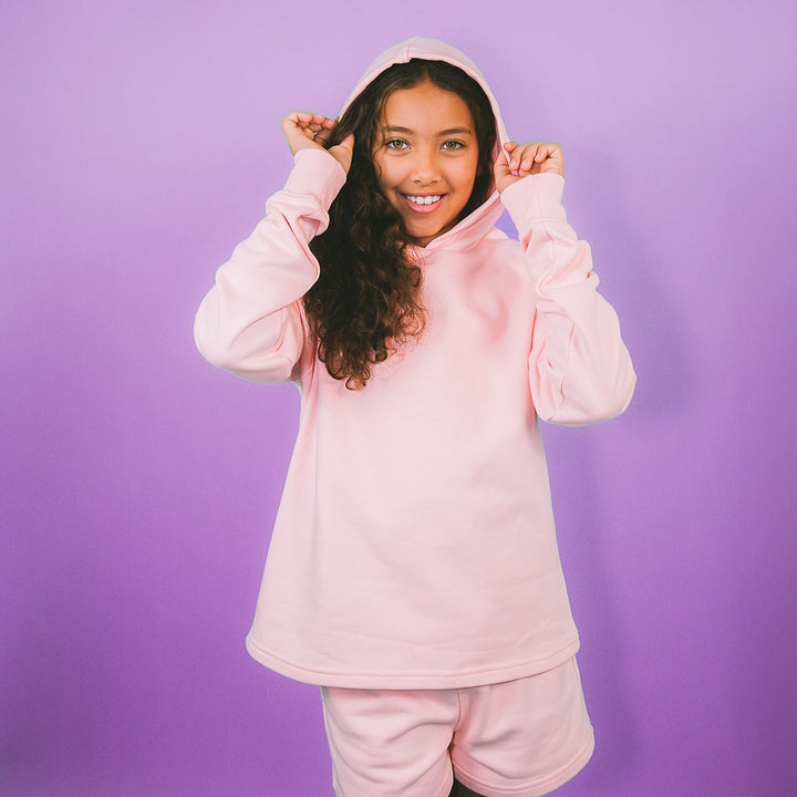 Smiling girl wearing a pink children's fashion hoodie set with long sleeves and matching shorts