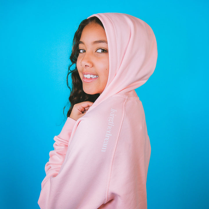Girl wearing a pink children's fashion hoodie set by dreamwithreem smiling against blue background