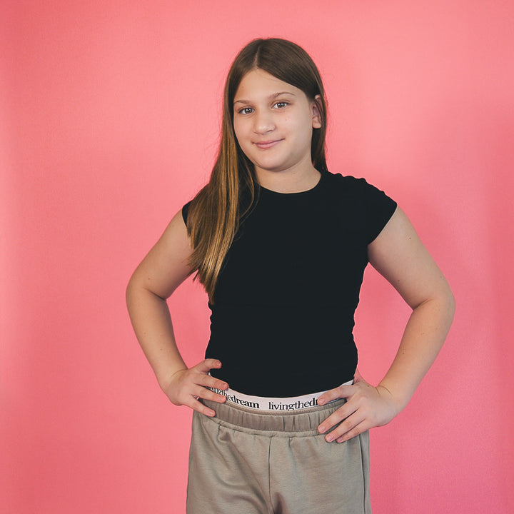 Girl wearing dreamwithreem comfortable camo shorts and black t-shirt standing against pink background