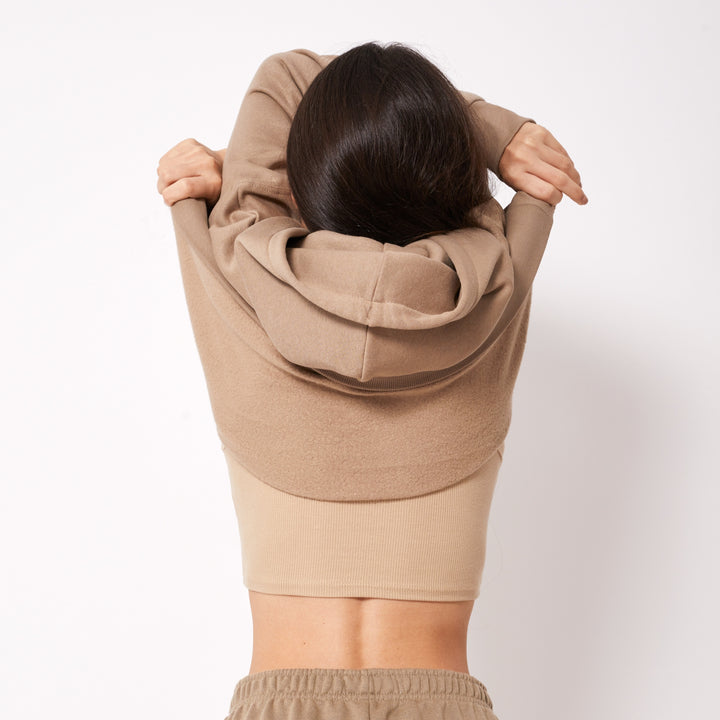 Woman putting on a beige personalized hoodie online for a stylish and cozy look
