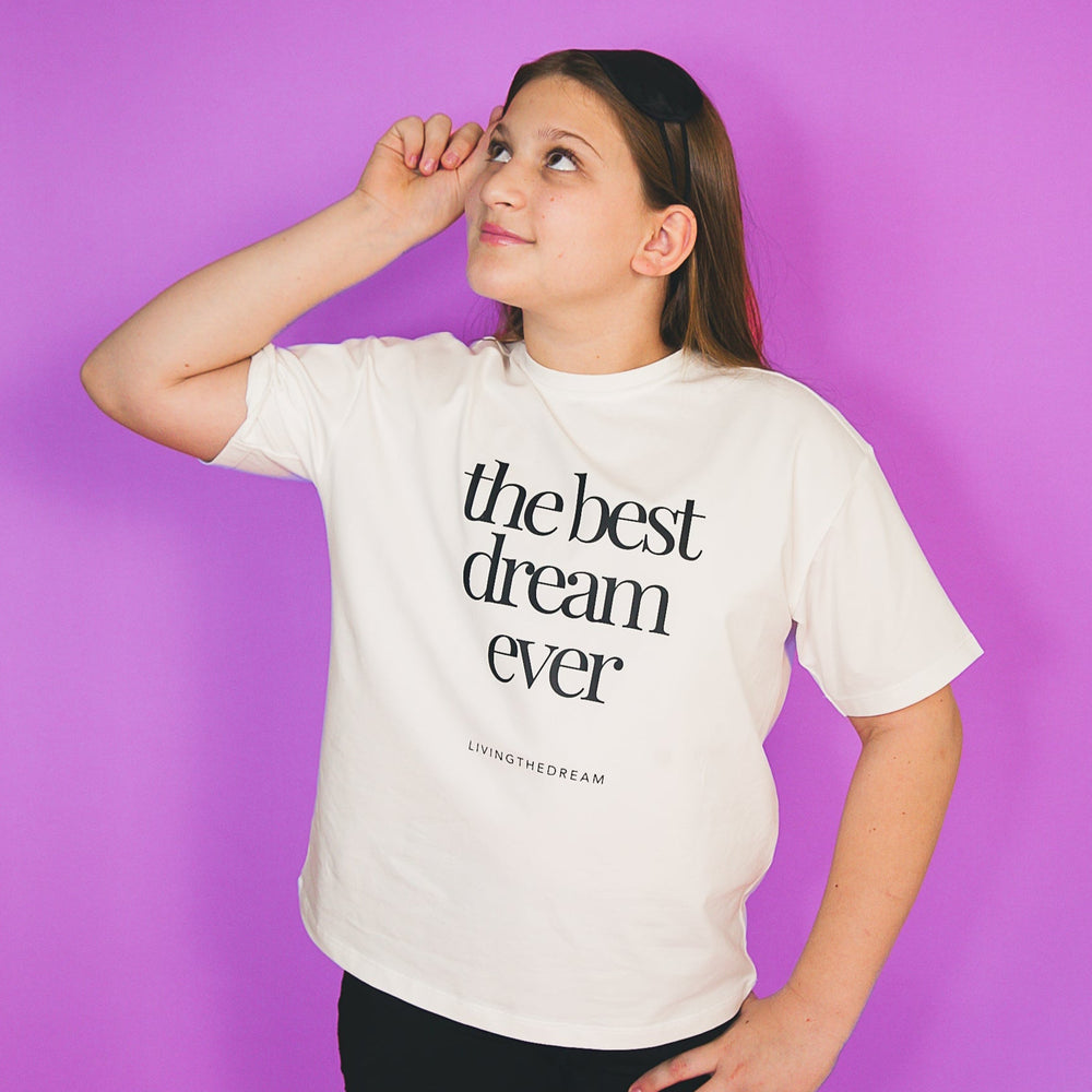 Kid wearing a white personalized statement shirts with the text the best dream ever on a purple background