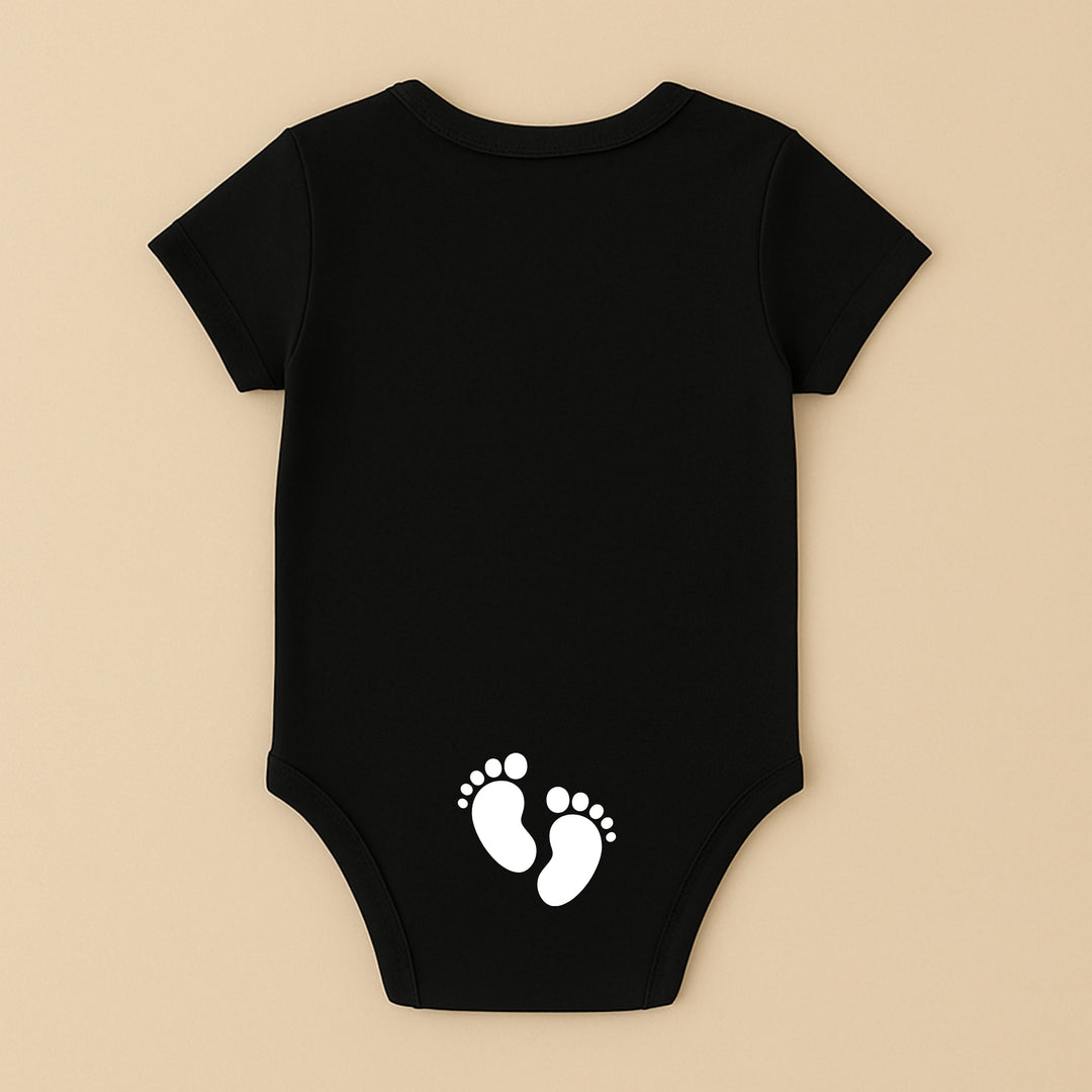 Black short sleeve personalized infant bodysuit with white baby footprints print on back on beige background