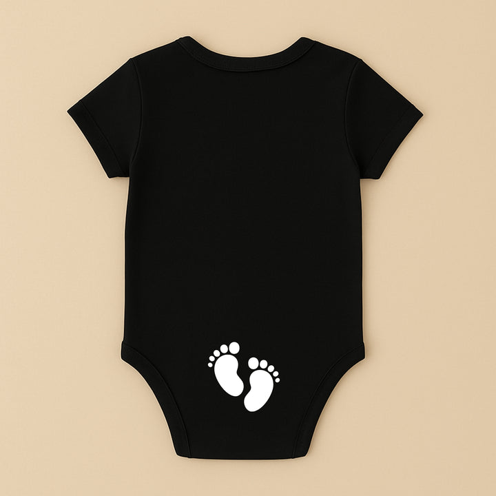 Black short sleeve personalized infant bodysuit with white baby footprints print on back on beige background