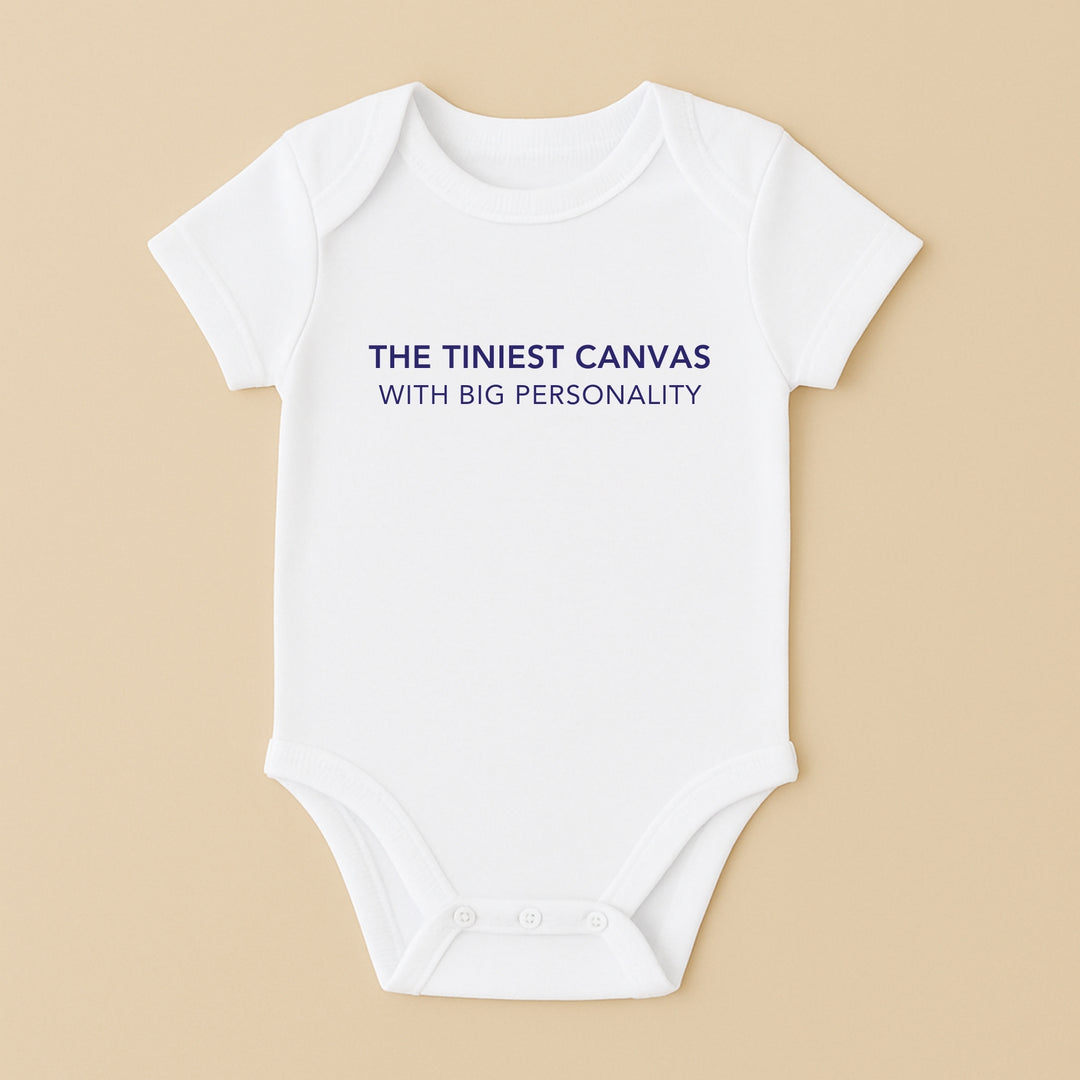 White short sleeve personalized infant bodysuit with navy slogan The Tiniest Canvas With Big Personality on beige background